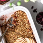 flat-lay image of dish with cranberry apple crumble topped with sliced apples with dried cranberries in a bowl