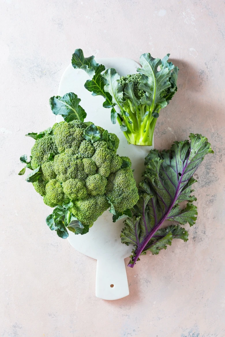 Broccoli and Kale leaves on a marble board. Healthy fresh green vegetables. Top view.