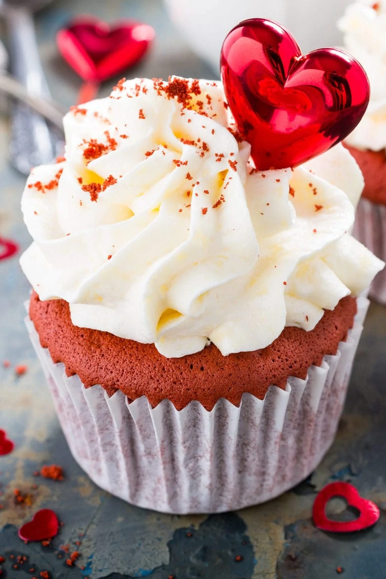 Delicious red velvet cupcakes decorated with hearts on rusty old metal background.