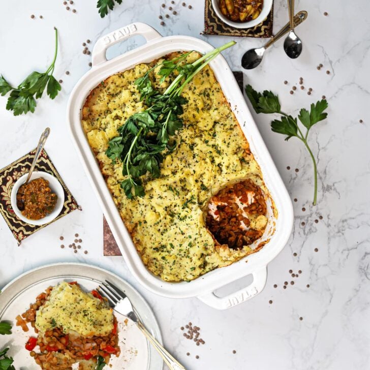 vegan Shepherd's pie in a white baking dish topped with fresh parsley with a portion served in a plate