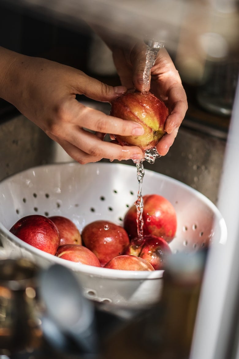 A person washing pomegranate under running water after her grocery trip