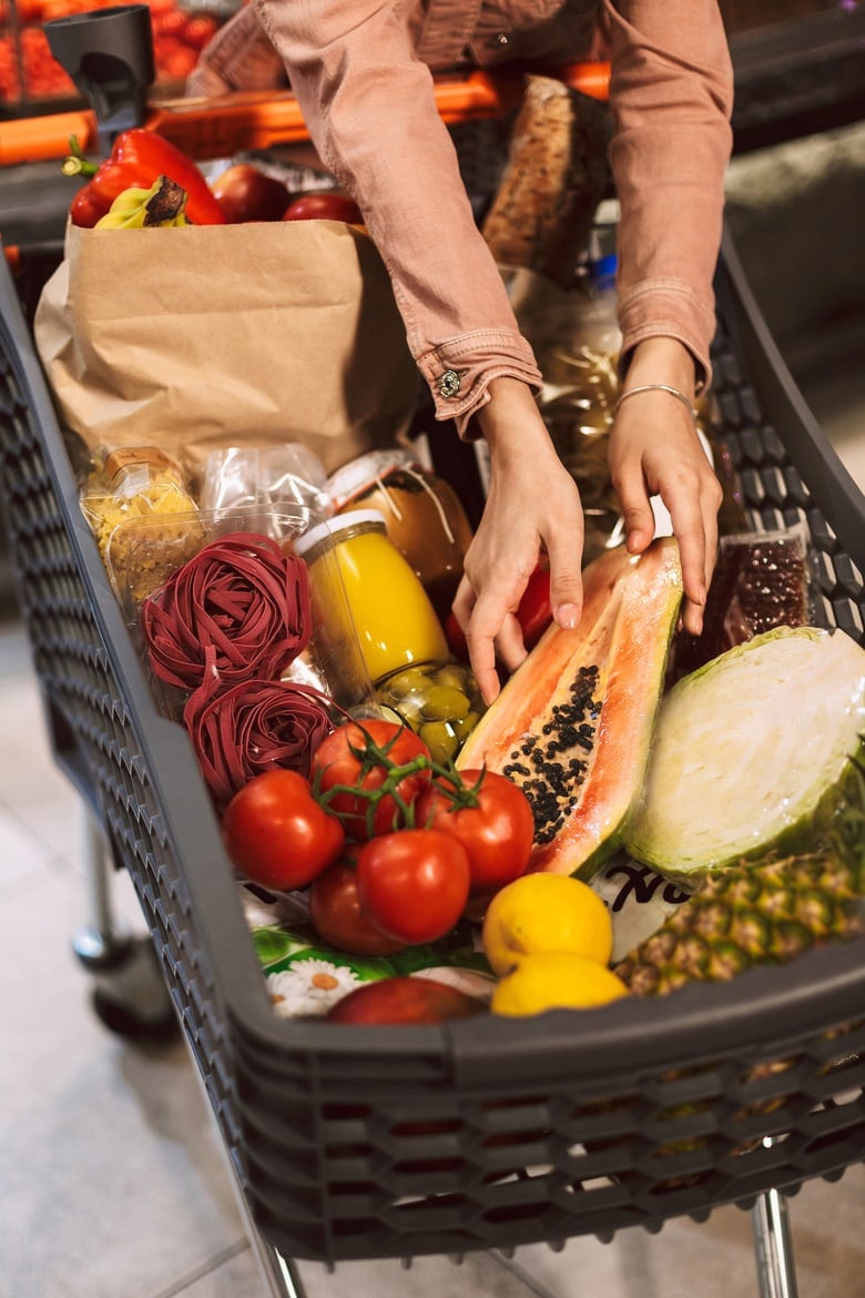 Close up trolley full of fresh products in modern supermarket. A women doing grocery shopping.