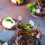 Traditional turkish tea with mint leaves and sweets in a traditional glass on a concrete background