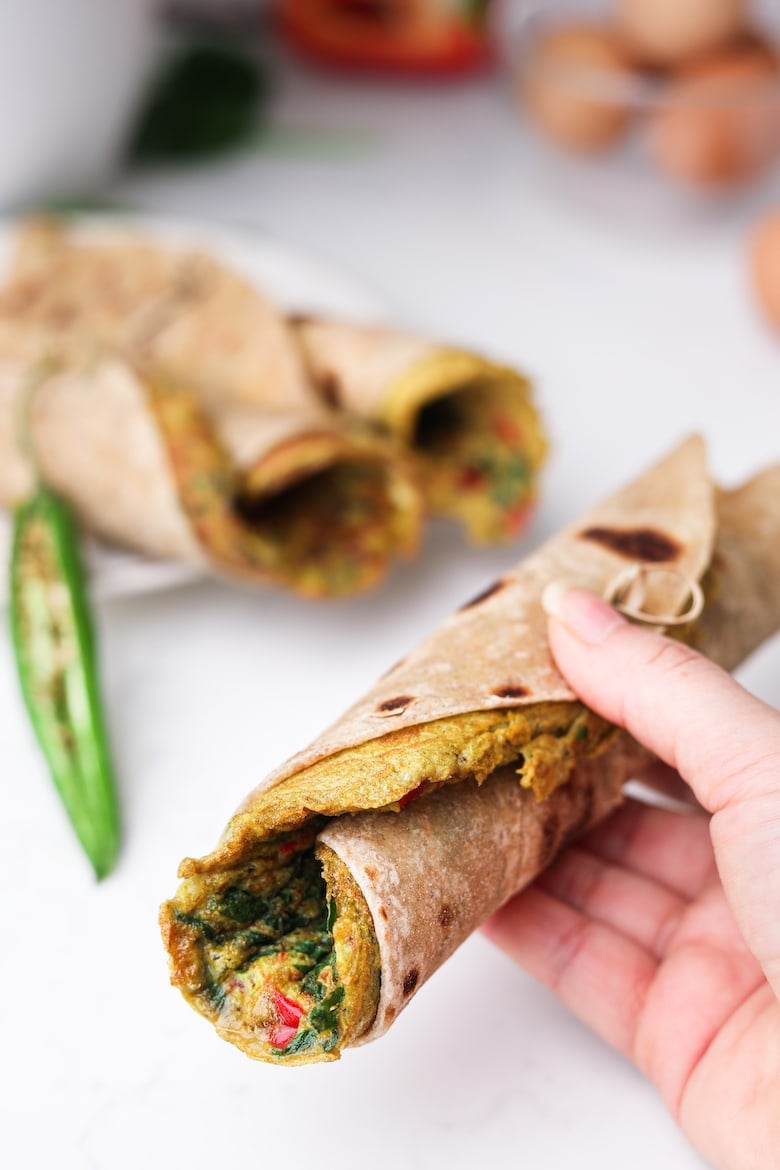 a hand holding an roti roll with a desi (south asian) omelette