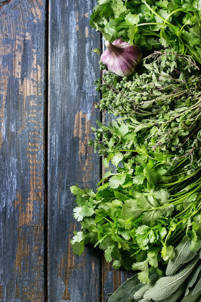 Variety of fresh organic herbs coriander, sage, oregano with garlic over old wooden plank background. Top view with copy space. Food background