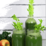 green juice in two mason jars and a bottle with celery stalks inside for decoration, surrounded by apples, kale and lime