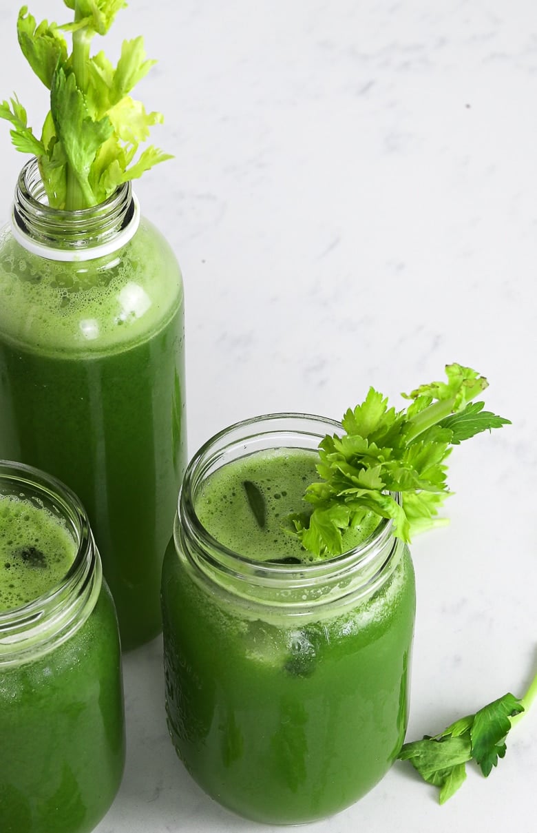 green juice in two mason jars and a bottle with celery stalks inside for decoration