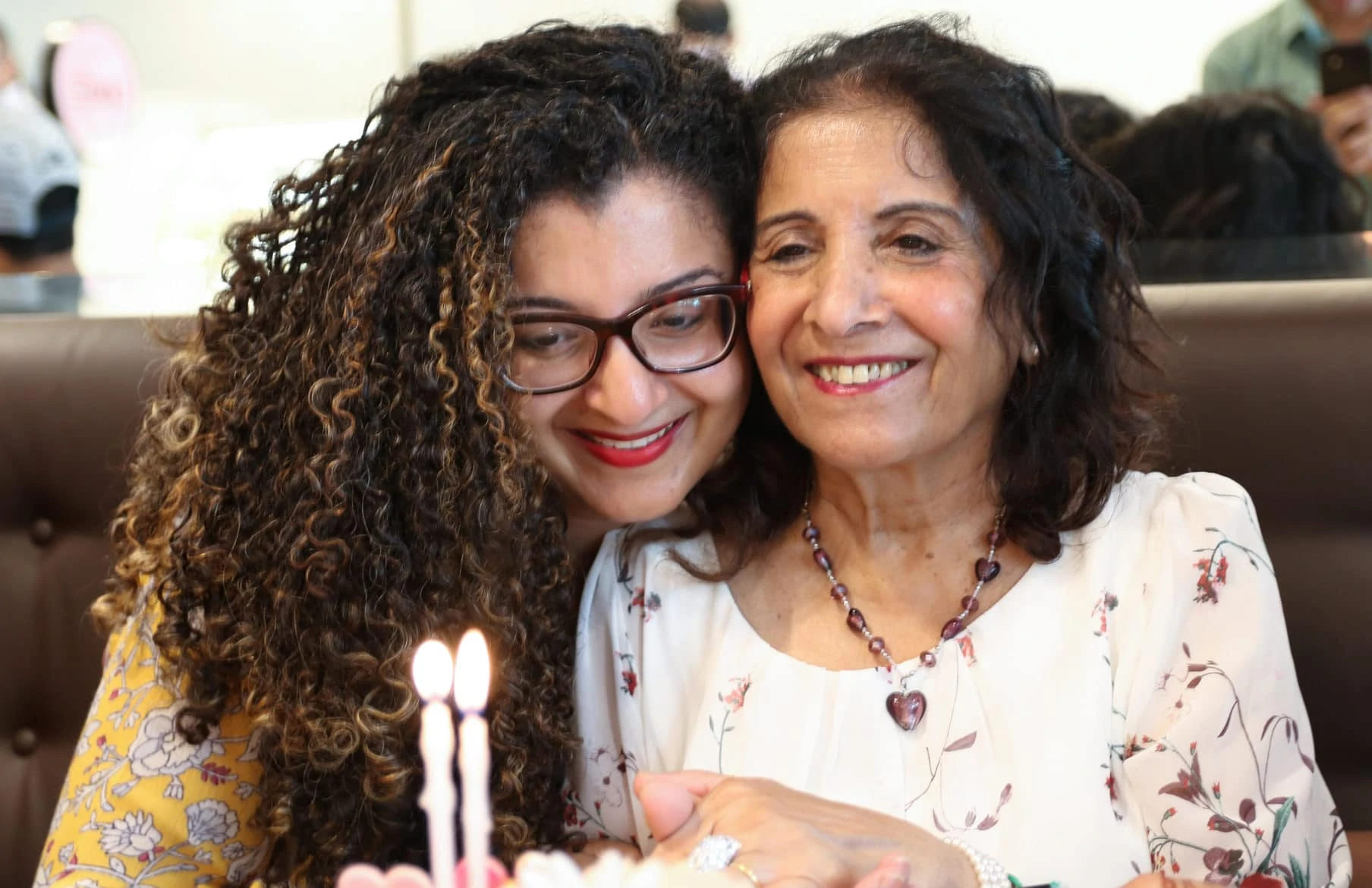 On Mother's Day, a mother and daughter snuggling in front of a cake with 2 candles
