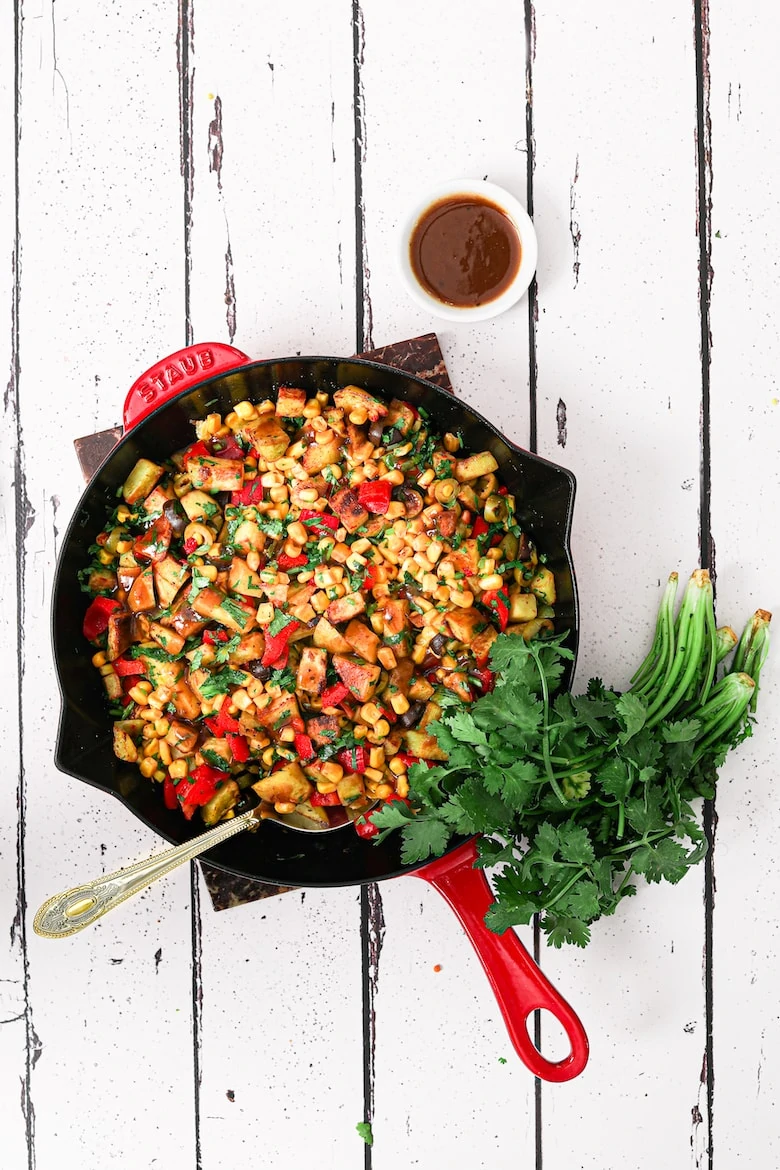 indian chaat salad with corn in a red staub pan with spoon in it
