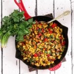 indian chaat salad with corn in a red staub pan with spoon in it and fresh cilantro on the side flat lay