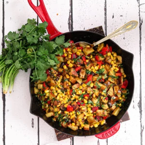 indian chaat salad with corn in a red staub pan with spoon in it and fresh cilantro on the side flat lay