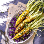 3 corn on the cob on a bed of purple cabbage placed on top of newspapers flatlay