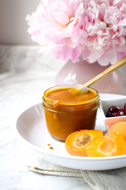 a small jar of BBQ peach sauce in a plate with peaches and pink flowers on the side