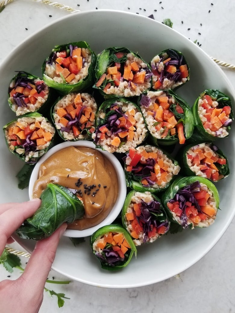 Bowl of collard green wraps stuffed with colourful vegetables and a peanut butter dip