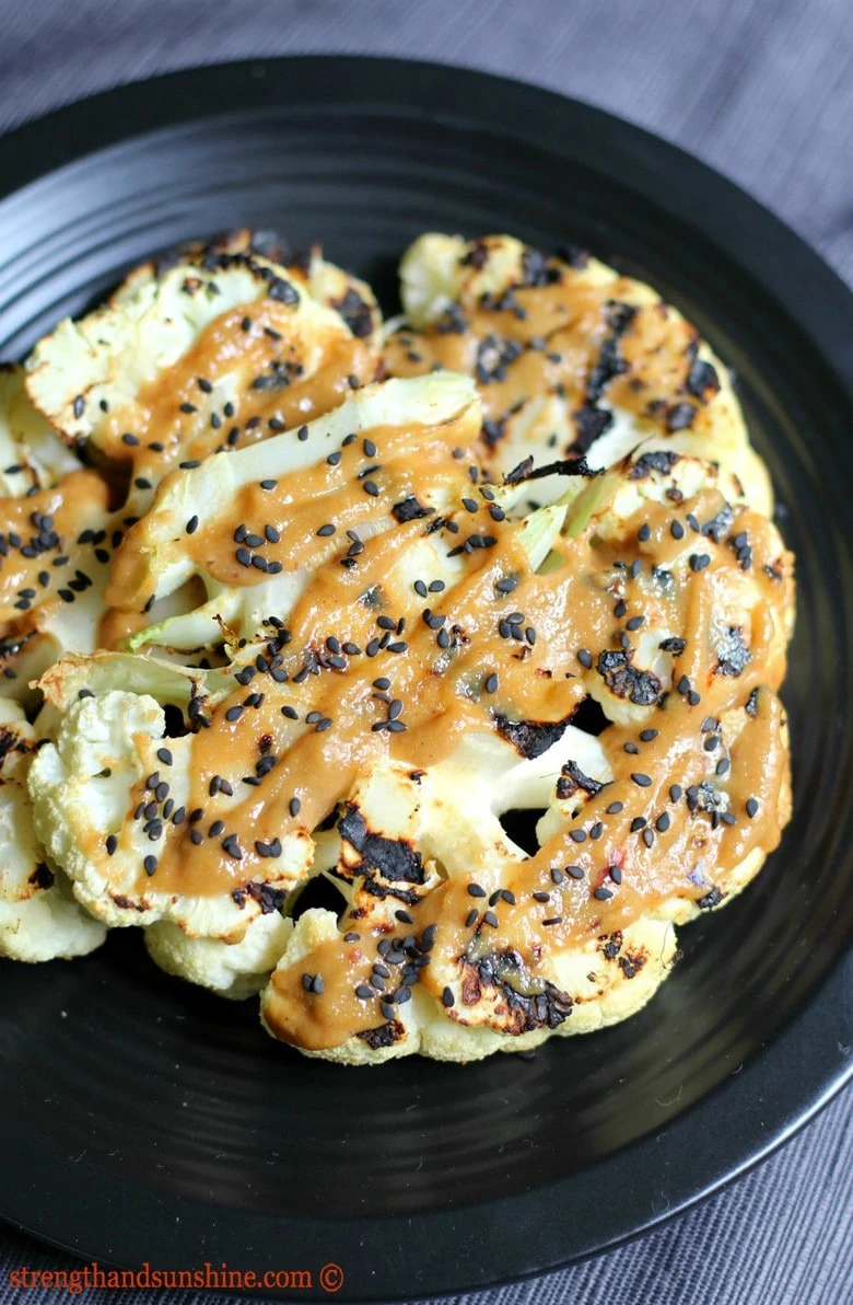 BBQ vegan recipe of cauliflower steak doused in tahini sauce on a black plate