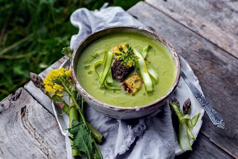 a bowl of green soup topped with asparagus shavings and croutons on a napkin