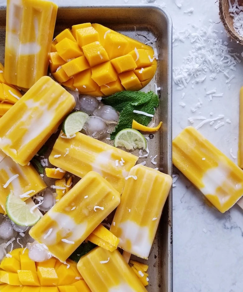 Tray of mango popsicles with ice and half a mango