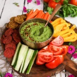 colourful platter of vegetables and crackers centred around a green avocado dip - perspective shot