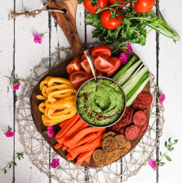 colourful platter of vegetables and crackers centred around a green avocado dip - flatlay