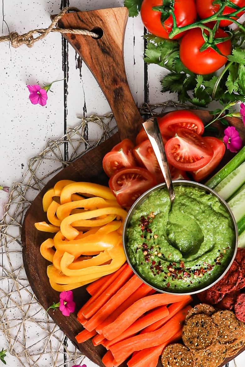 colourful platter of vegetables and crackers centred around a green avocado dip - flatlay