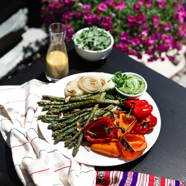 plate of grilled asparagus, colourful bell peppers and onion on a tables outside surrounded by pink flowers