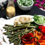 plate of grilled asparagus, colourful bell peppers and onion on a tables outside with a side green salad and a bottle of dressing