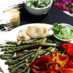 plate of grilled asparagus, colourful bell peppers and onion on a tables outside with a side green salad and a bottle of dressing