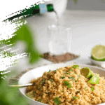 a bowl of cooked quinoa garnished with cilantro leaves and lime wedges with a a glass of sparking water in the background.