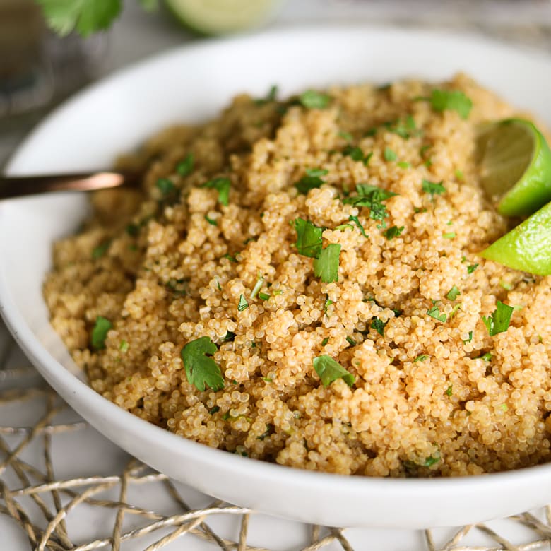 a bowl of cooked quinoa garnished with cilantro leaves and lime wedges