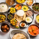a selection of bowls of a variety of Indian dishes arranged in a circle