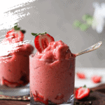 side shot: Two glasses filled with scoops of strawberry nice cream topped with fresh strawberries and displayed on a wooden board
