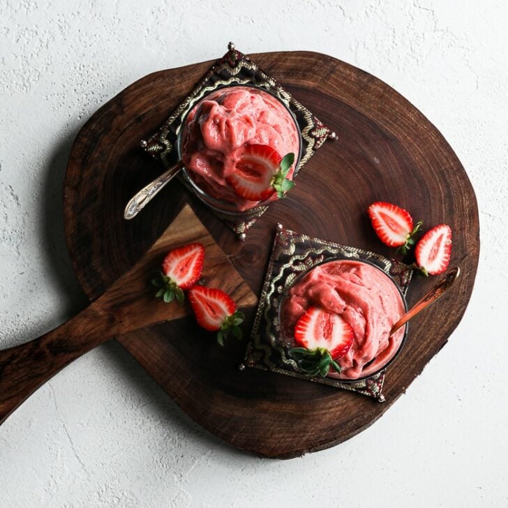 flat-lay: two glasses filled with scoops of strawberry nice cream topped with fresh strawberries and displayed on a wooden board