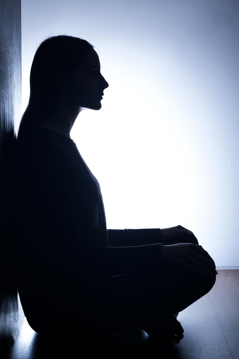 Girl in darkness, sitting on floor back to wall