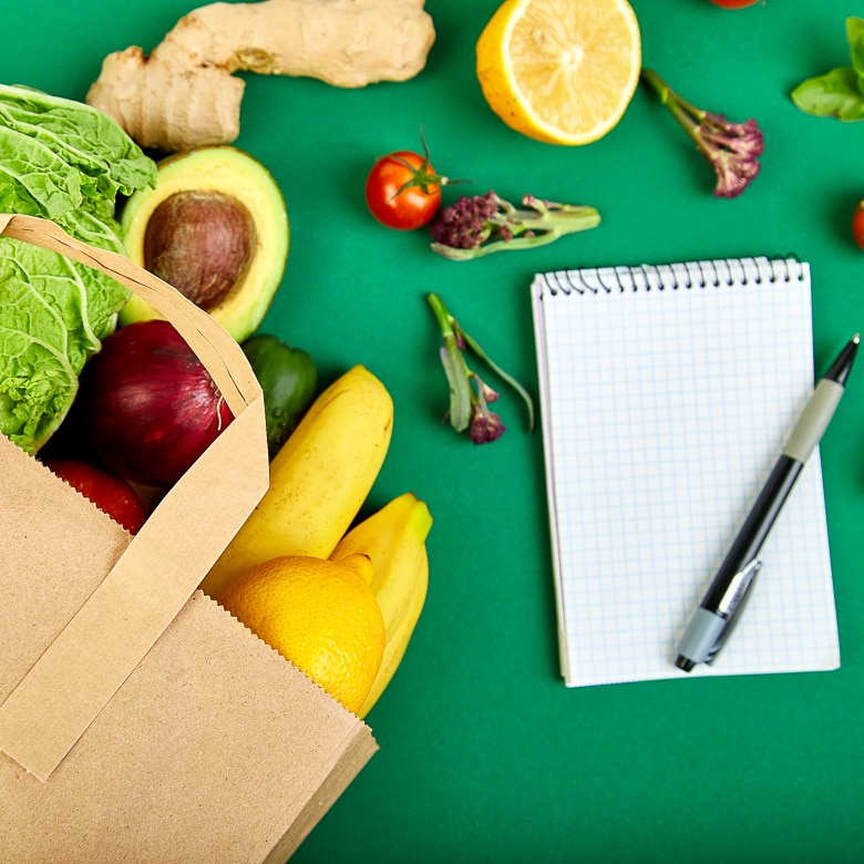 Shopping list, recipe book, diet plan. Grocering concept. Full paper bag of different fruits and vegetables, ingredients for healthy cooking on a color background. healthy food. Diet or vegan food, vegetarian. Top view. Flat lay.