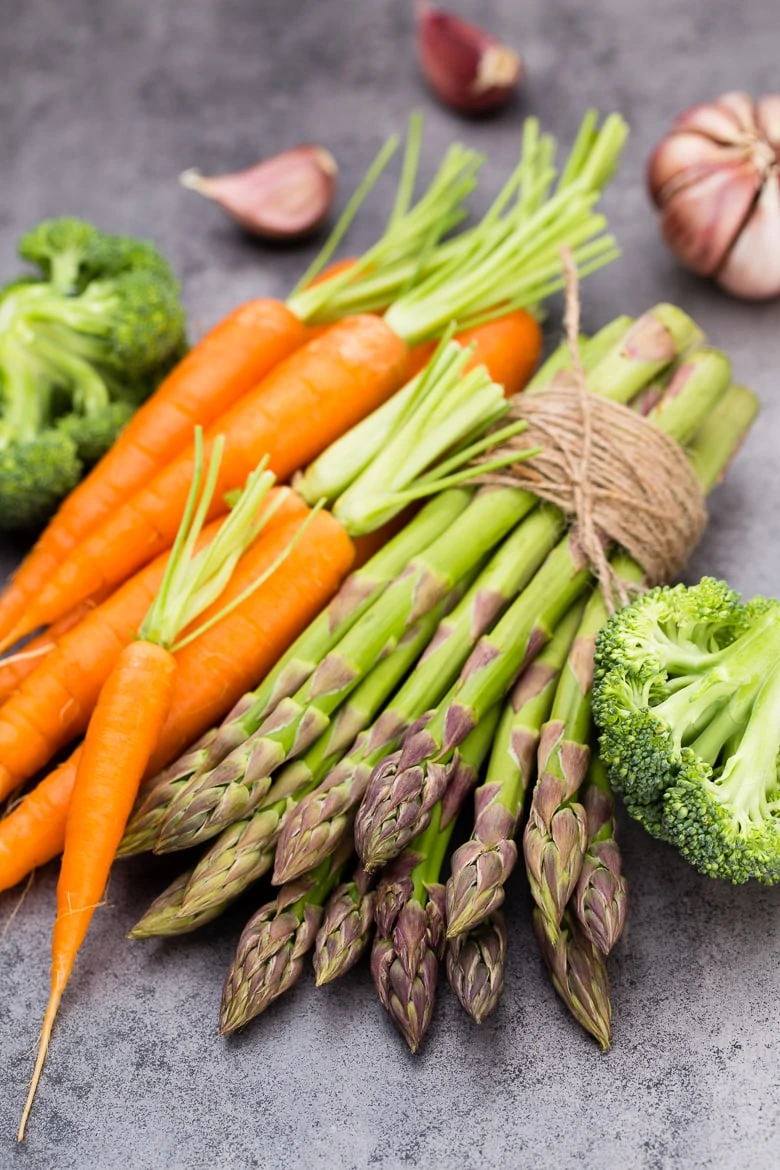 Banches of fresh green asparagus, and vegetables on wooden background, top view