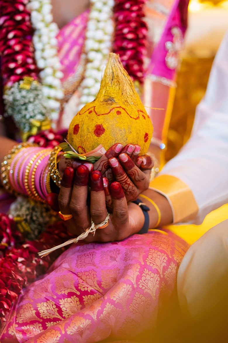 indian bride and groom on their wedding day holding a yellow coconut