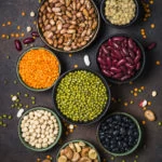 Legumes, lentils, chikpea and beans assortment in different bowls on stone table. Top view vertical.