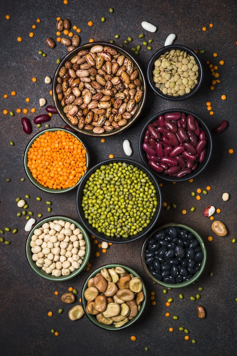 Legumes, lentils, chikpea and beans assortment in different bowls on stone table. Top view vertical.
