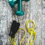 Green dumbbells and jump rope on vintage background. Top view.
