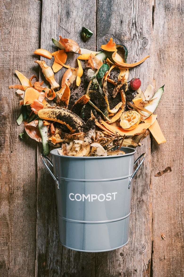 Sustainable and zero waste living. Vegetable waste in recycling compost pot. Top view. Copy space. Peeled vegetables on chopping board, white compost bin on blue background. Recycle kitchen waste