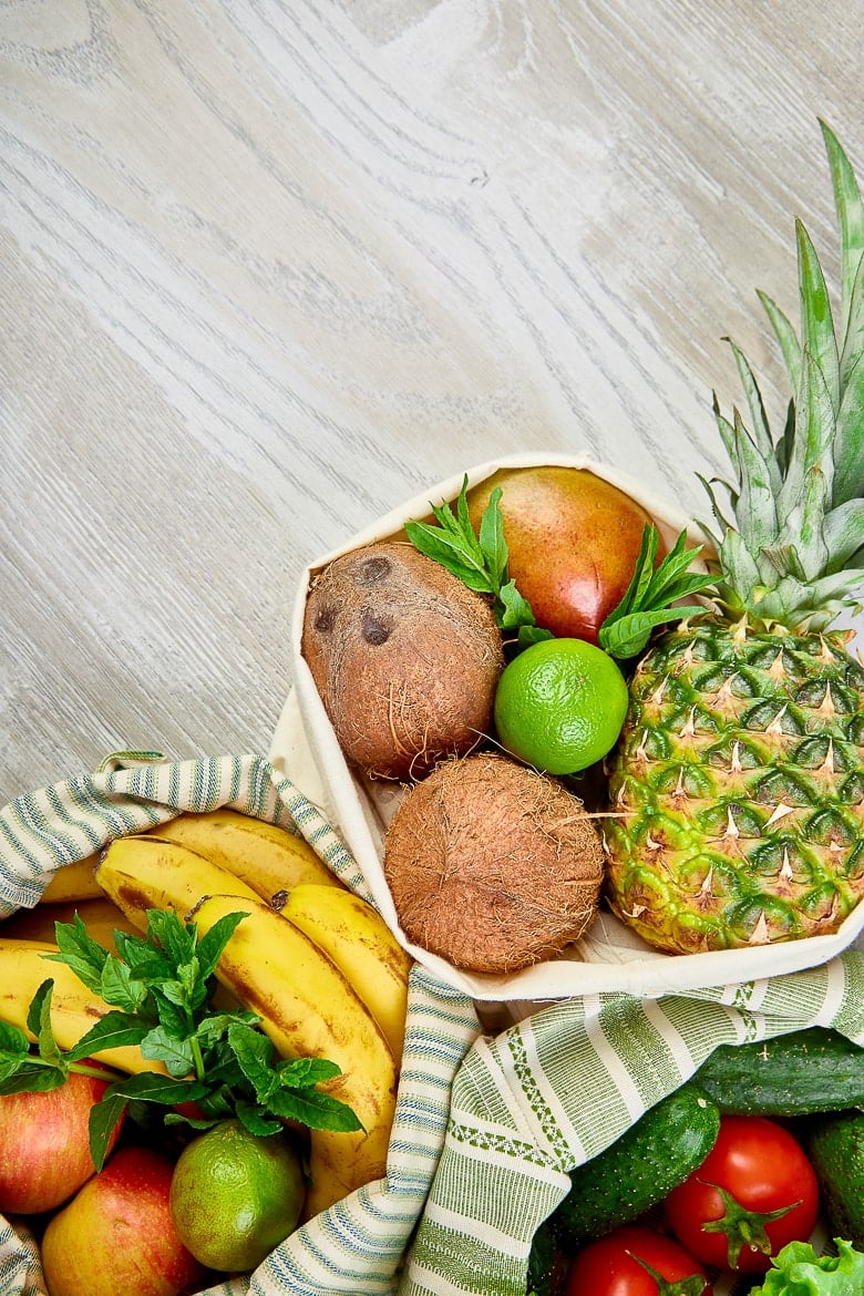 Fresh vegetables and fruits in eco cotton bags on table in the kitchen. Flat lay, top view. Zero waste, plastic free lifestyle concept. Healthy veggie food diet and detox.