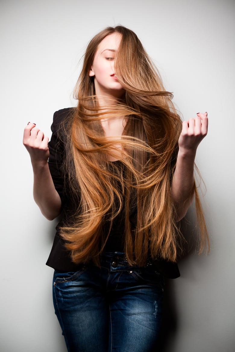 Girl dressed in black jacket, with long flowing hair, posing with her head turned to side against white wall