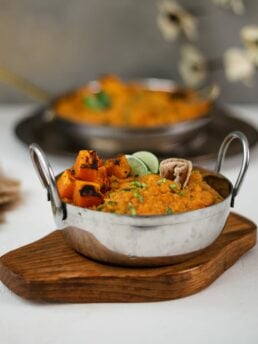Two bowls of yellow daal topped with squash and limes wedges placed on trays