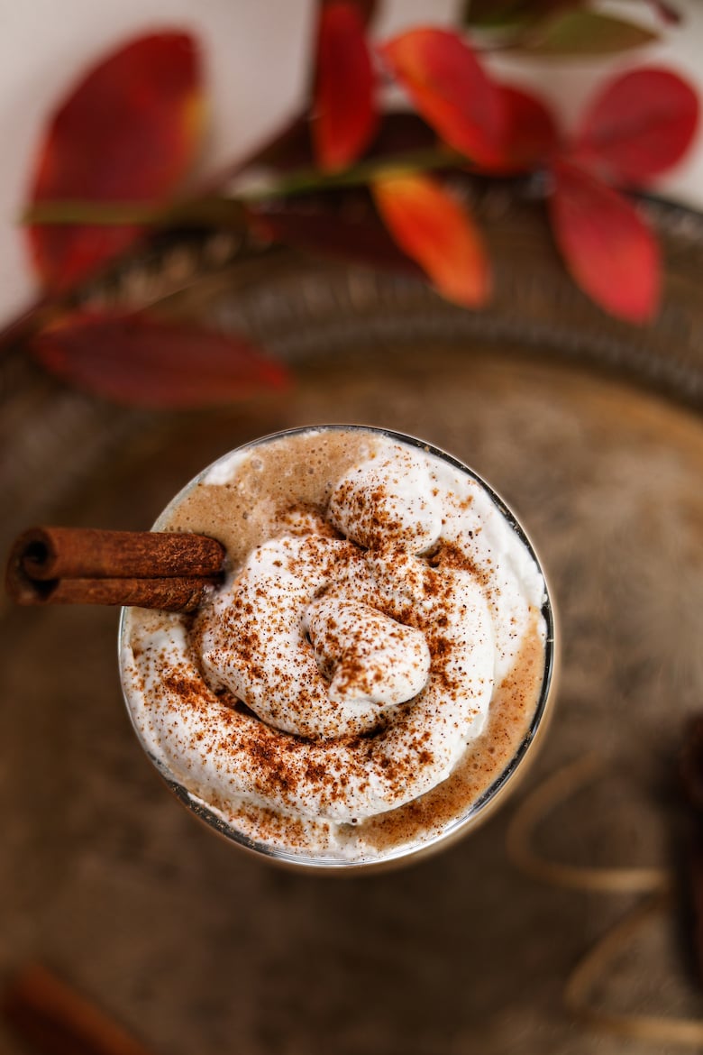 flatlay shot of the top of a glass with whipped cream sprinkled with cinnamon displayed on a tray,