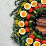 a low carb appetizer created as a edible holiday wreath, made with boiled eggs and vegetables on skewers on a bed of herbs - flatlay