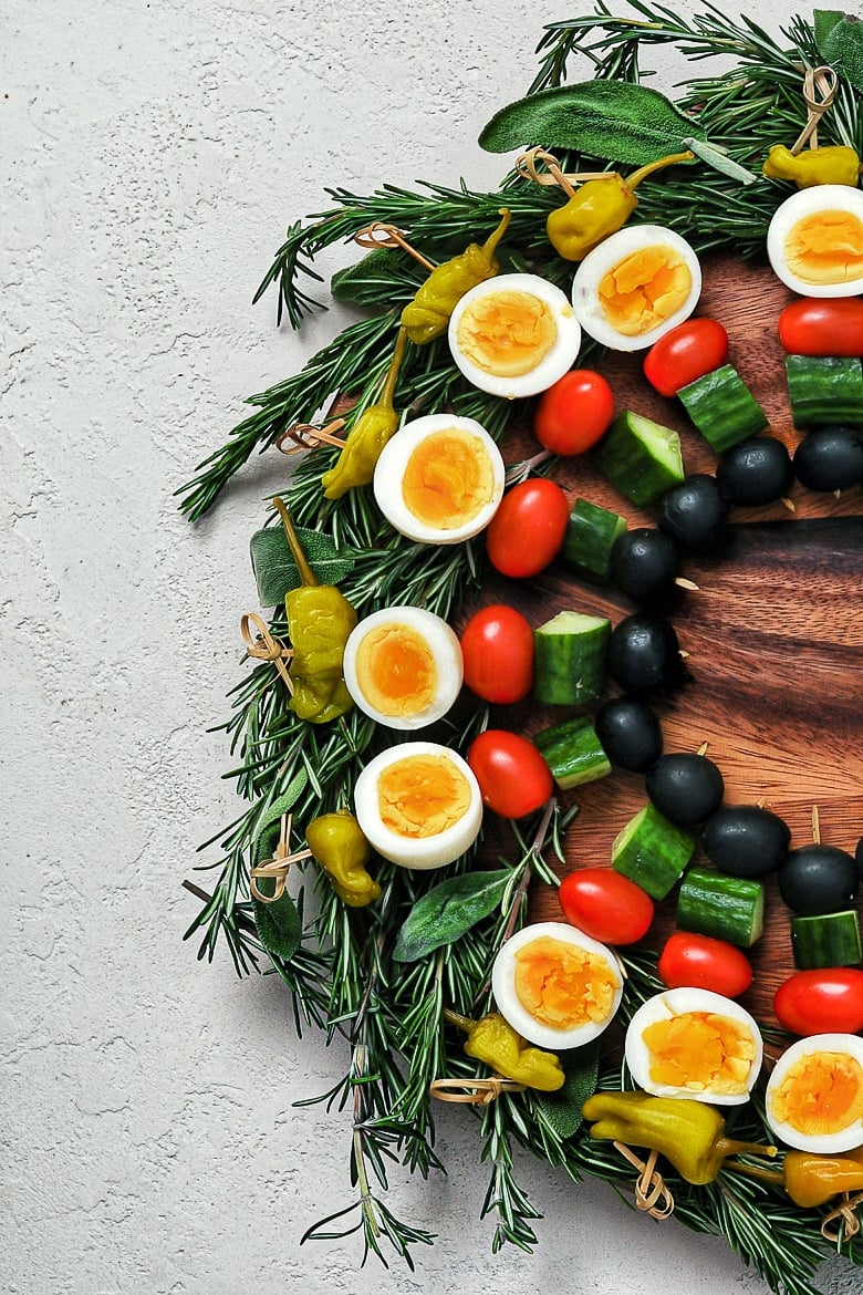 a low carb appetizer created as a edible holiday wreath, made with boiled eggs and vegetables on skewers on a bed of herbs - flatlay