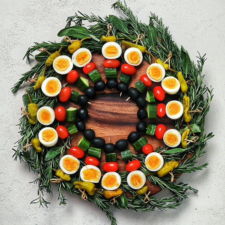 an edible holiday wreath made with boiled eggs and vegetables on skewers on a bed of herbs - flatlay