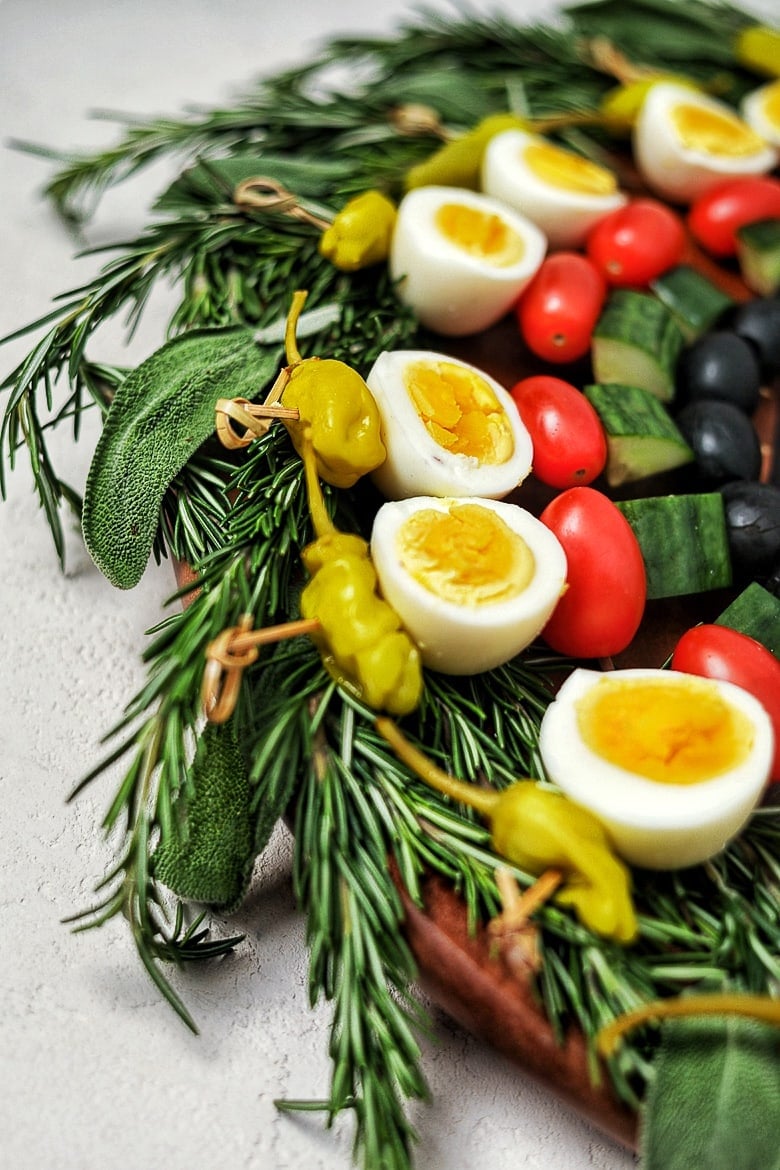 a low carb appetizer created as a edible holiday wreath, made with boiled eggs and vegetables on skewers on a bed of herbs