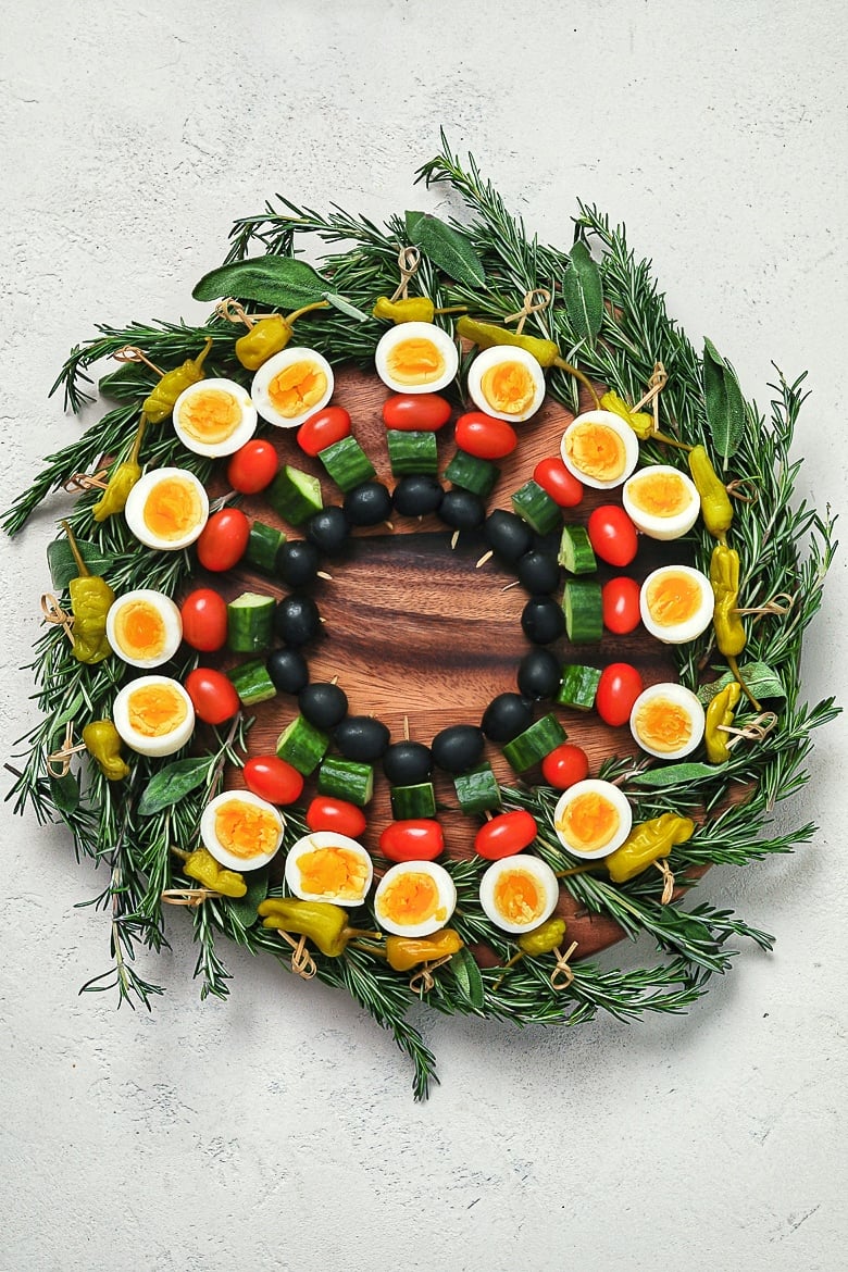 an edible holiday wreath made with boiled eggs and vegetables on skewers on a bed of herbs - flatlay.