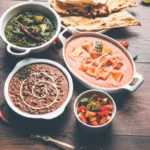 bowls of desi food dishes (indian cuisine) on a wooden table with naan bread